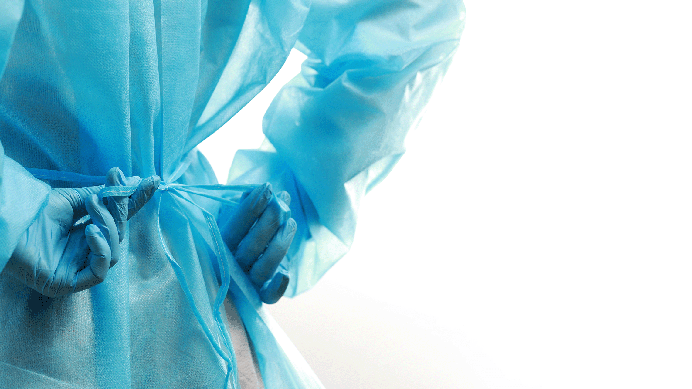 Gloved person tying PPE gown