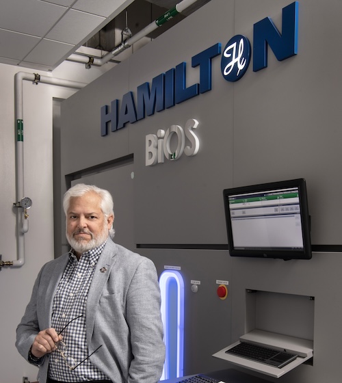 Dr. McCarty standing in front of the Hamilton BiOS sign and computer