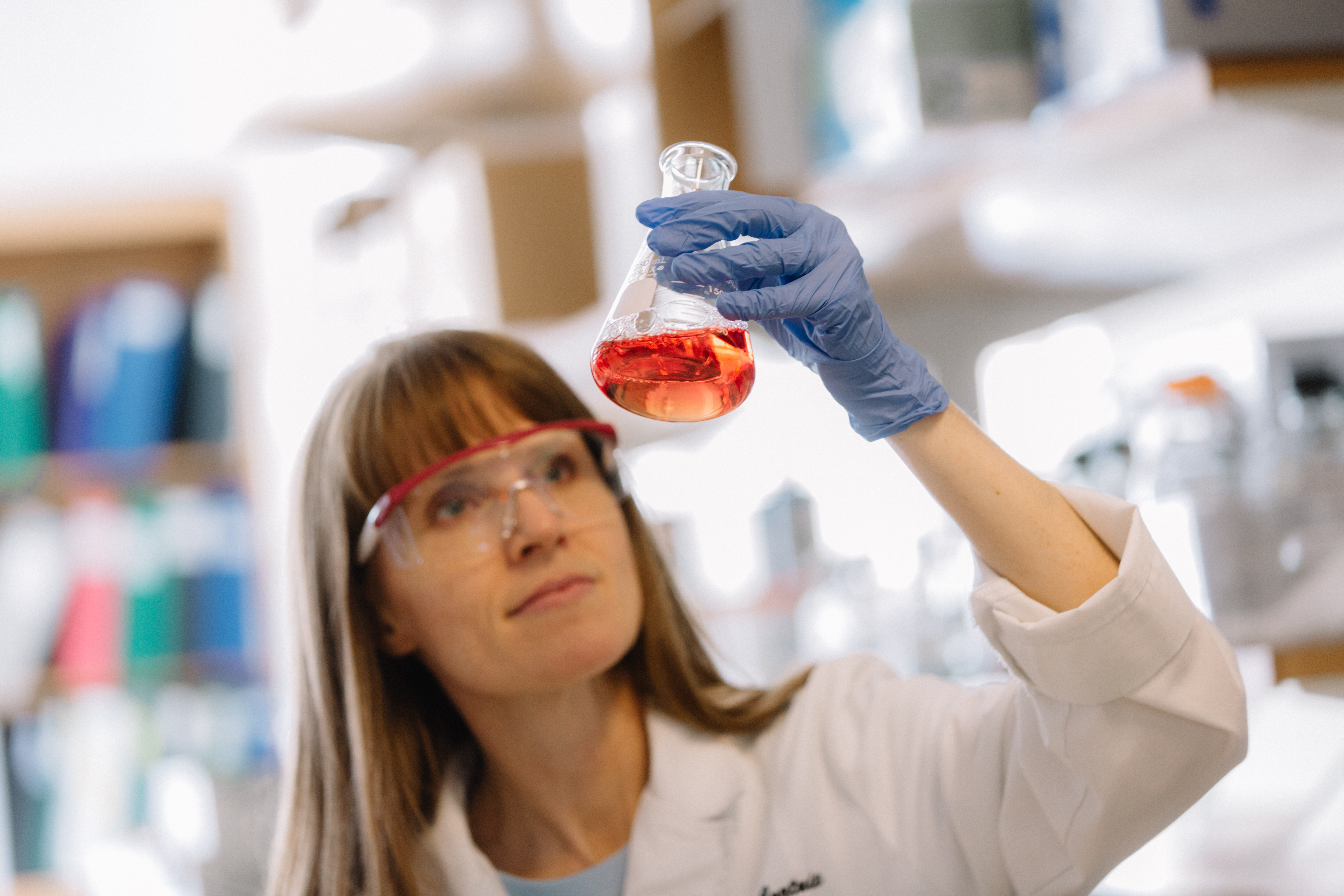 Researcher holds up beaker filled with orange liquid